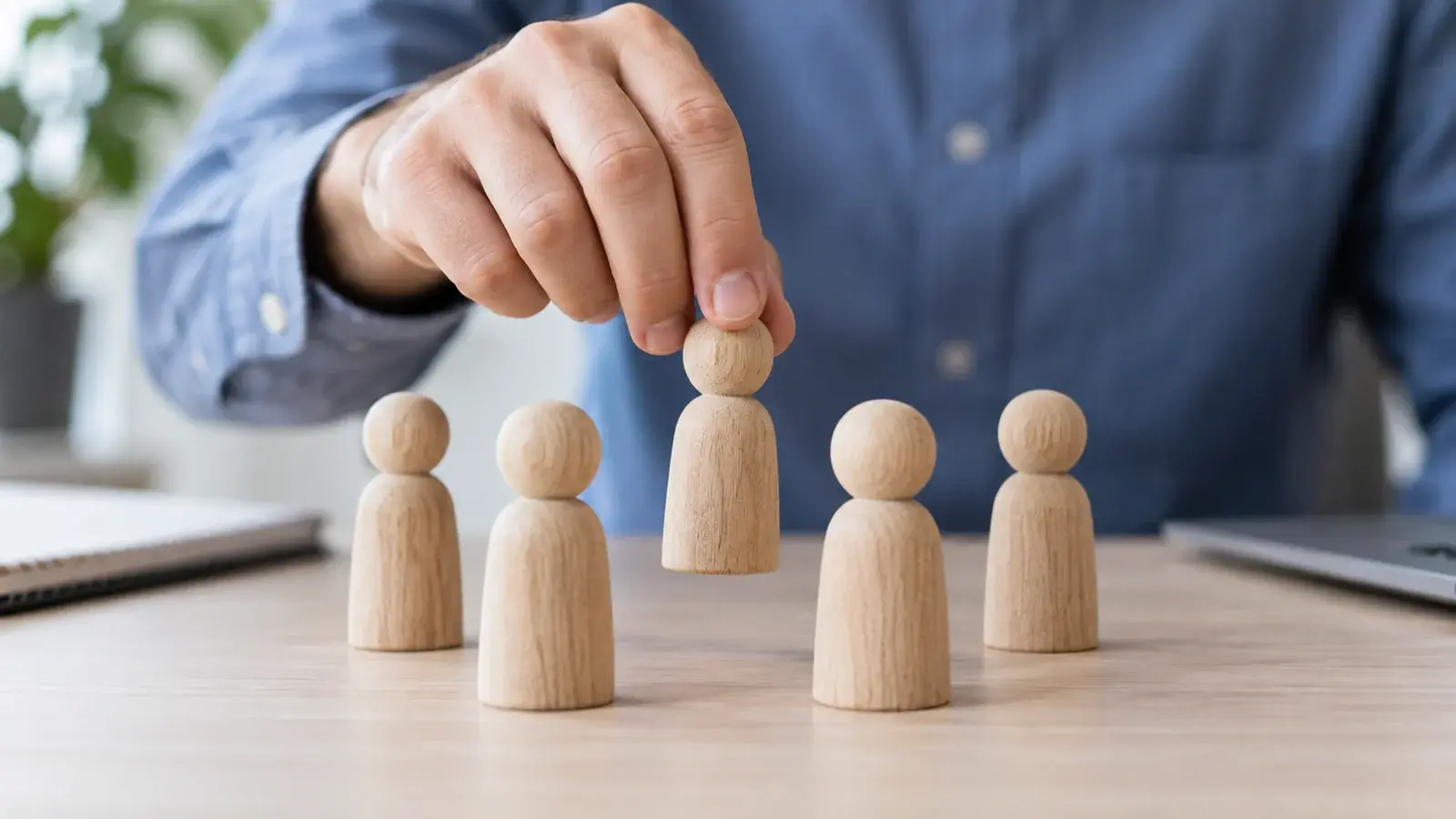 A recruiter selects a wooden person figure from a group on a desk.