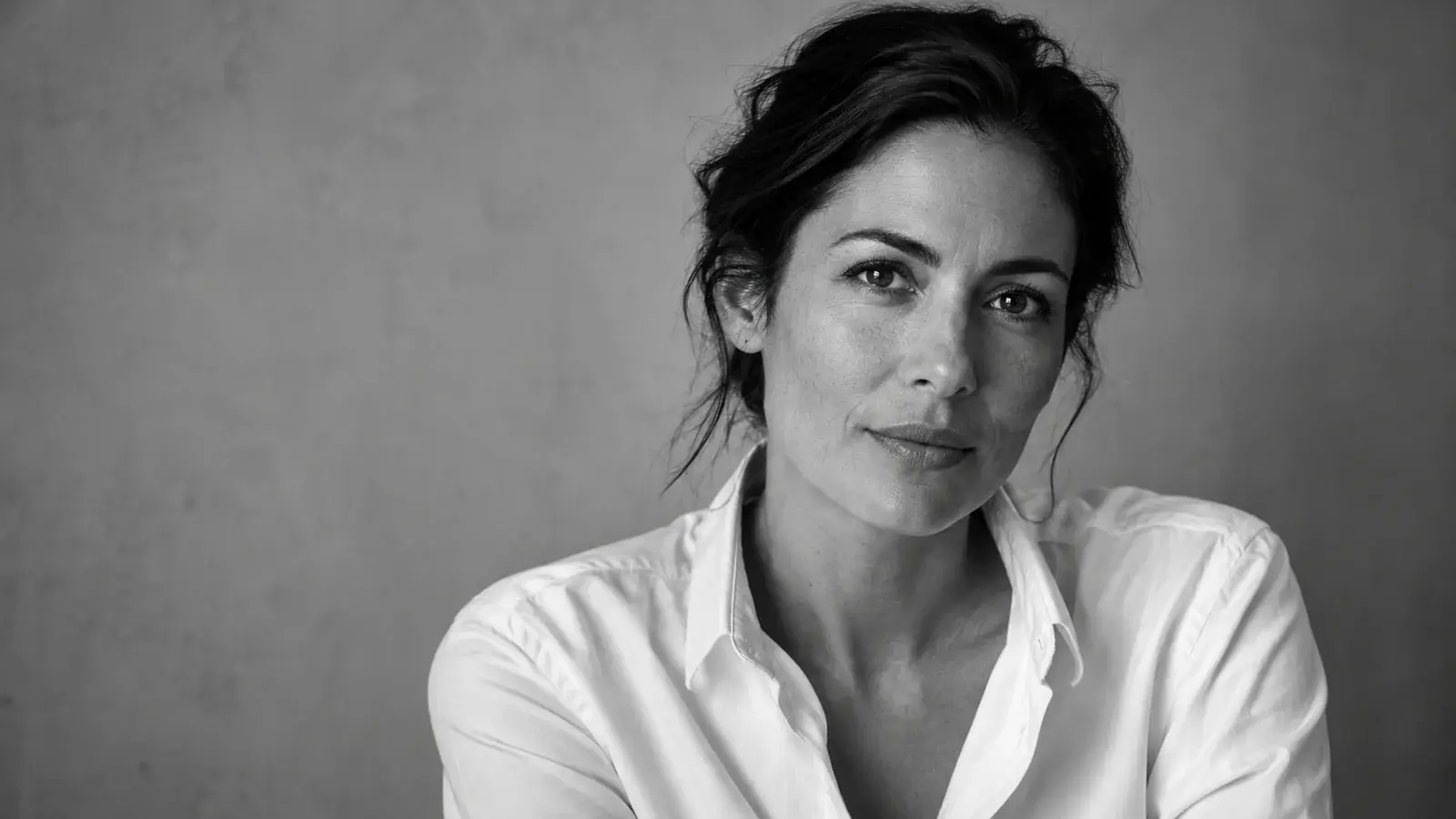 A thoughtful woman in a white shirt poses in a black-and-white portrait.