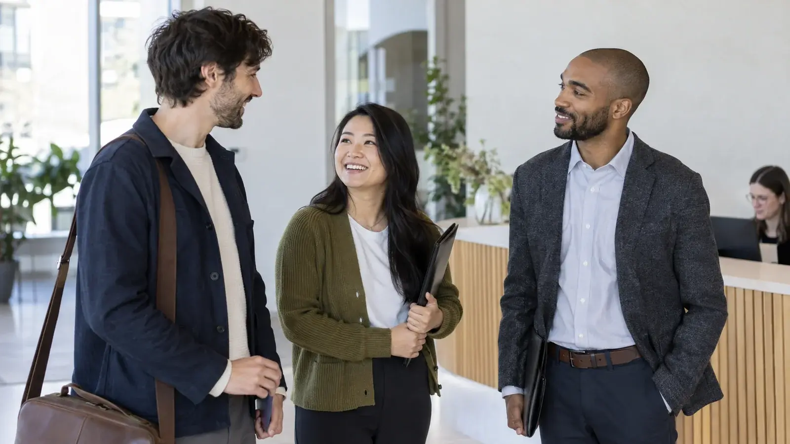 Three job candidates share a light conversation near an office reception desk.