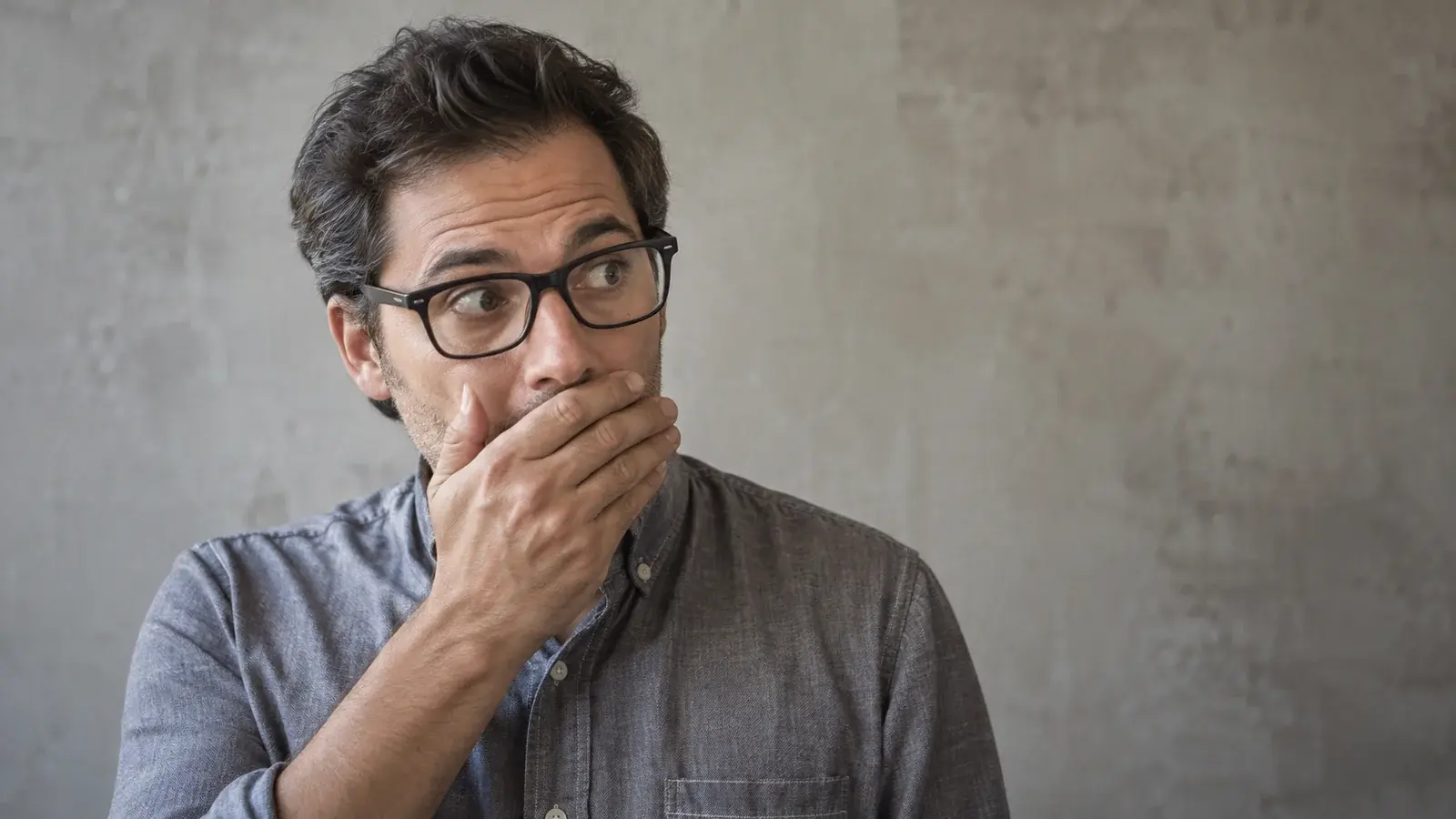 A man in glasses pauses with one hand over his mouth.