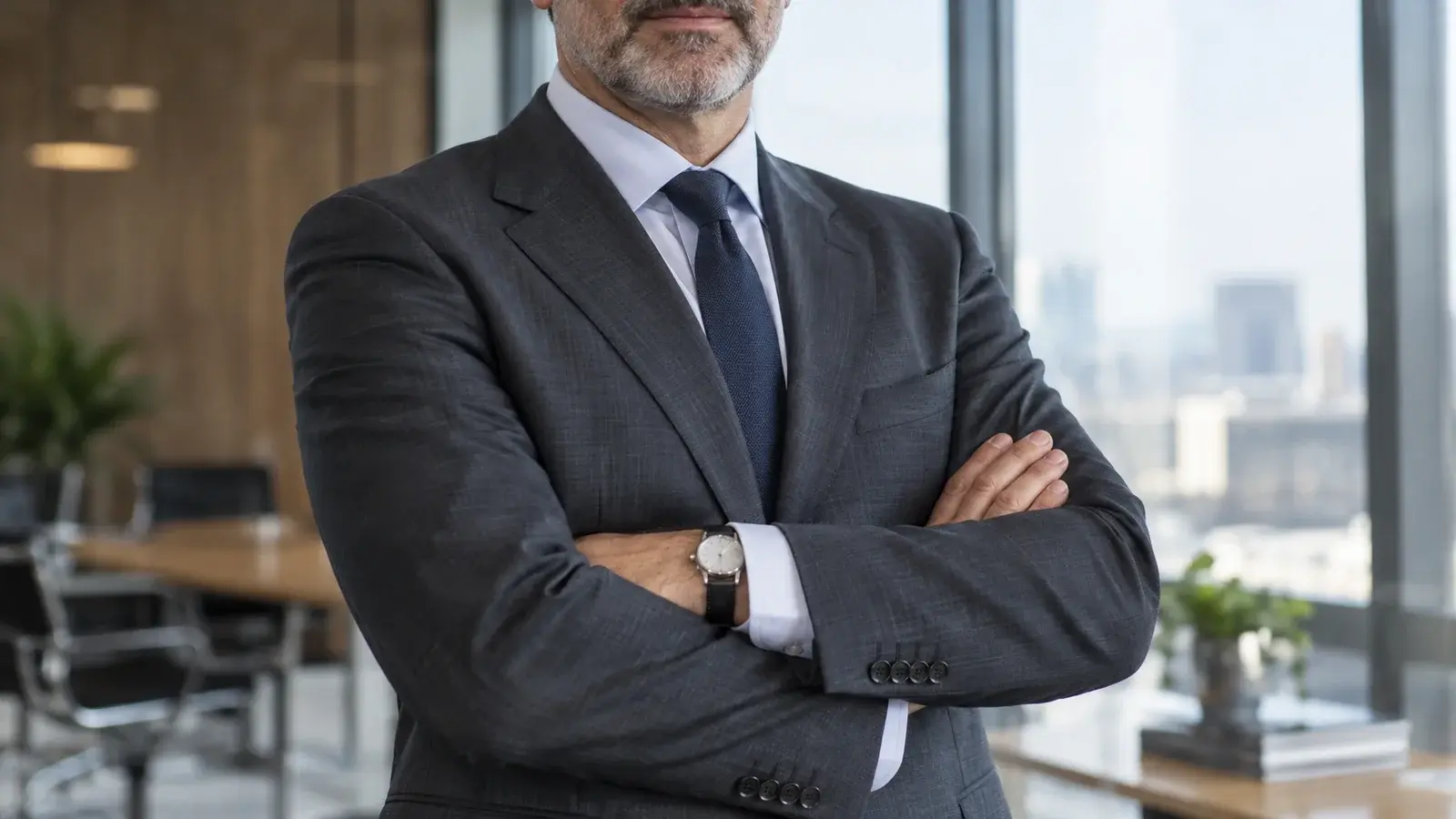 A manager stands with folded arms in a charcoal suit.
