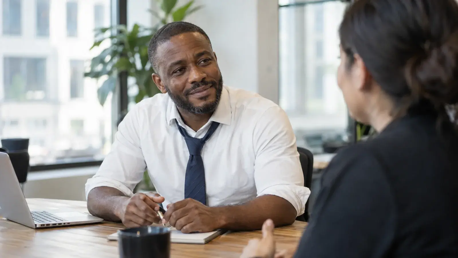 A sales coach listens to a colleague across an office table.