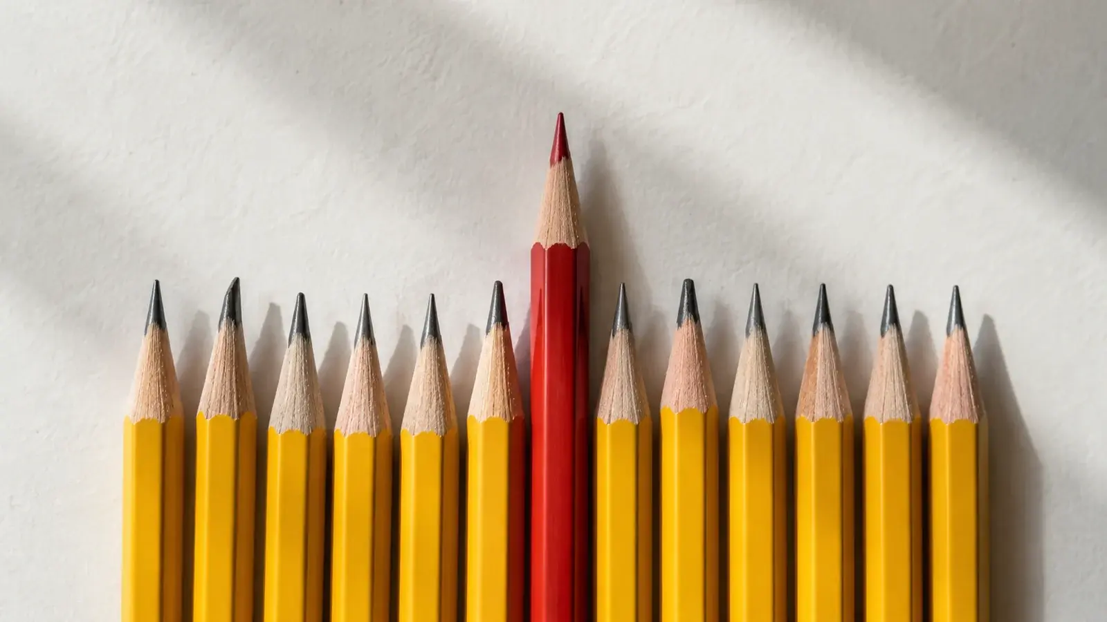 One red pencil extends beyond a row of yellow pencils.