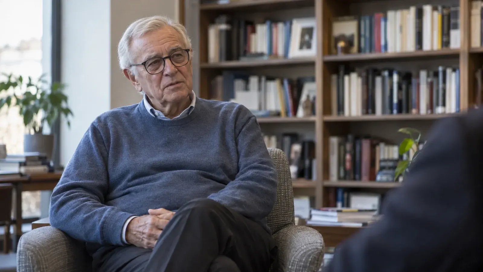 An older professional listens with a reserved expression during an interview.