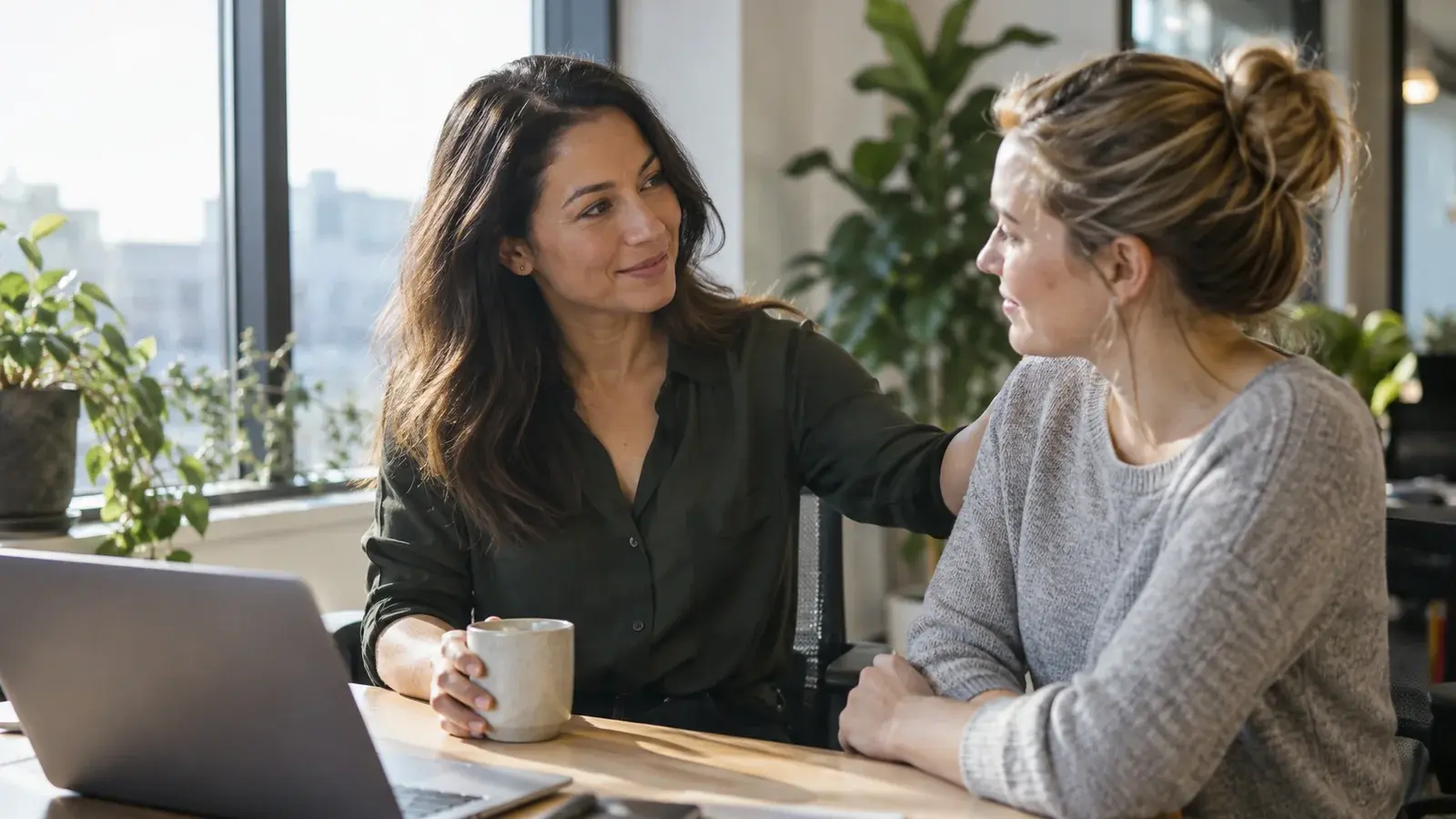 A team leader offers encouragement to a colleague beside a window.