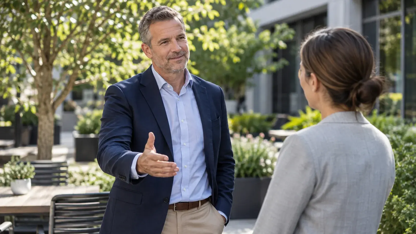 A sales coach makes a welcoming gesture during a conversation outdoors.