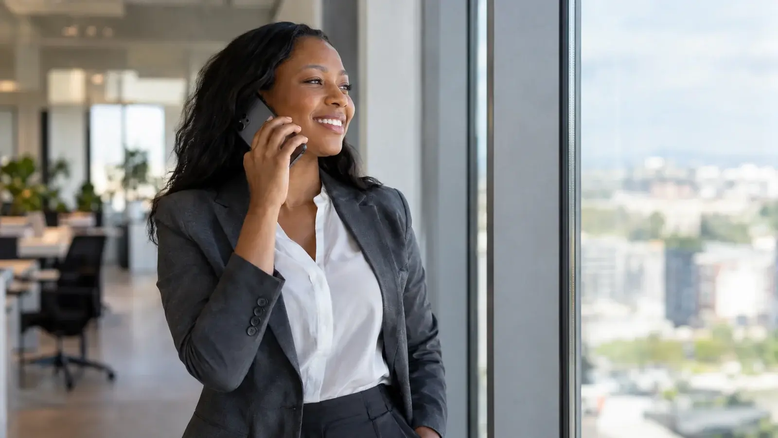 A sales manager speaks on her phone beside an office window.
