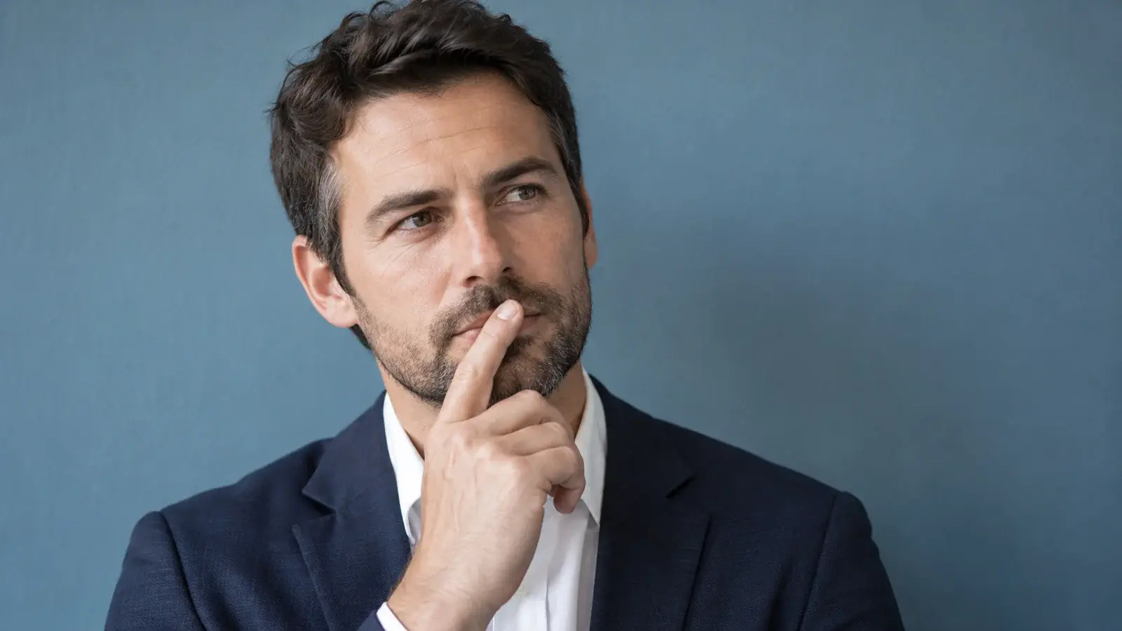 A professional pauses thoughtfully with a finger near his lips.